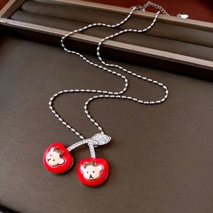Close-up of red enamel cherry pendant necklace featuring cartoon bear and sparkling leaf