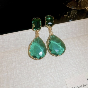 Macro shot of green teardrop crystal earrings in gold setting with emerald cut details