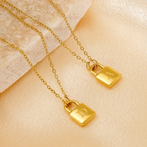 Detail of gold titanium steel necklaces with lock pendants featuring letters A and D