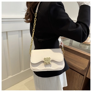 Detail of cream saddle bag with wave edges and gold bear-shaped lock closure