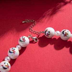 Acrylic snowman and pearl beaded necklace with lobster clasp against red background
