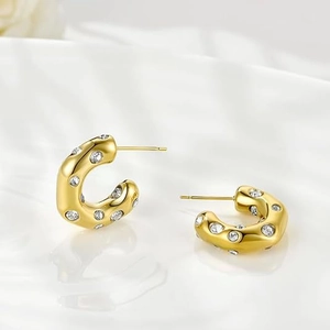 Macro detail of gold C-shaped hoop earrings with hammered texture and clear cubic zirconia