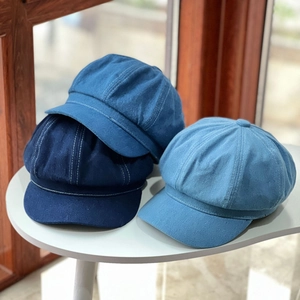 Three shades of denim newsboy caps stacked on a white table with visible stitching