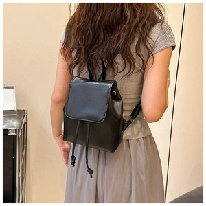 Back view of a black faux leather backpack with drawstring closure on a model