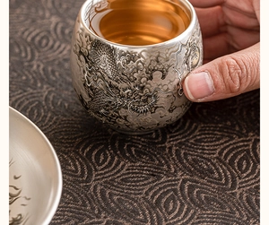 Gros plan d'une main tenant une tasse en argent avec motif de dragon sculpté