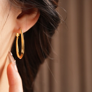 Close-up of a model wearing a gold twisted round hoop earring with minimalist metal design