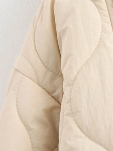Macro view of cream quilted cotton jacket showing circular stitching and windproof fabric