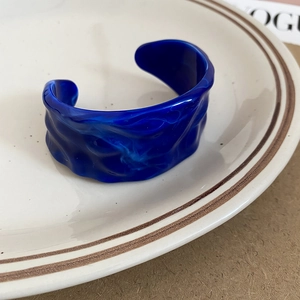 Macro detail of dark blue acrylic cuff bracelet with wavy texture on a ceramic plate