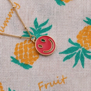 Detail of a gold-plated necklace featuring a red enamel smiley face pendant on a summer cloth