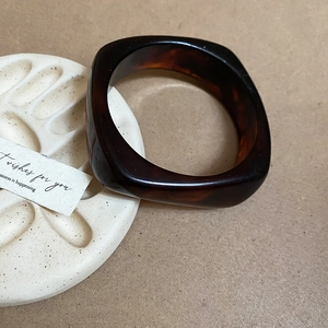 Detail shot of a square resin bangle with dark brown tortoiseshell texture on a white stand