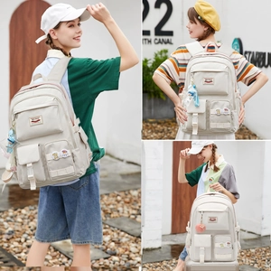 Detail of cream multi-pocket backpack with cute plush ball charms and decorative badges