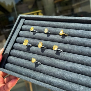 Close-up of assorted yellow gemstone rings in various cuts on a black velvet display tray