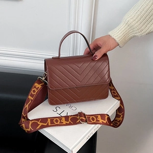 Detail of dark brown handbag with V-shaped quilting and vintage jacquard wide strap