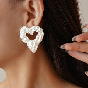 Dettaglio di orecchini a cuore con trama irregolare su modella con finitura argento