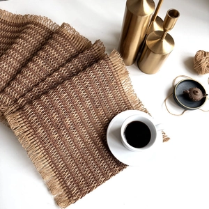 Detail of bohemian woven table runner with natural jute fringe and rustic earth tones