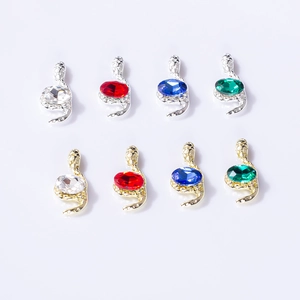Macro detail of snake-shaped nail art charms with vibrant gems and micro-inlaid crystals