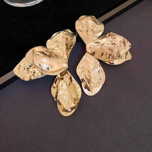 Macro shot of large golden petal earrings with irregular hammered metal texture details