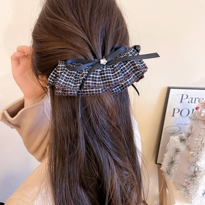 Close-up of a vintage plaid fabric bow hair clip worn on long hair in a home setting