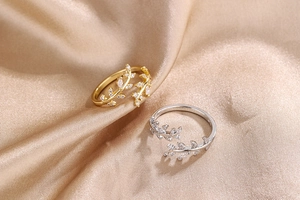 Detailed view of olive leaf rings with white zircons in gold and silver on satin