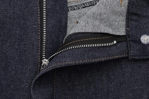 Detail of dark indigo denim jeans with silver zipper, yellow stitching, and fabric texture