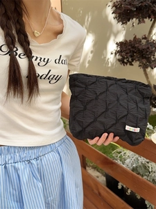 Quilted black pouch with geometric texture and colorful label held by a model