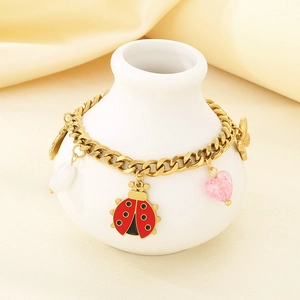 Close-up of gold chain bracelet with cute ladybug and butterfly charms on white vase