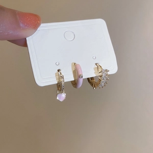 Détail de trois boucles d'oreilles dorées avec pendentif cœur rose, anneau émail et zircons