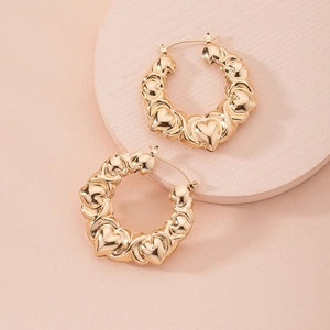 Macro detail of gold C-shaped hoop earrings featuring a layered relief heart pattern