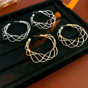 Detail view of gold and silver twisted hollow C-shaped hoop earrings on dark leather background