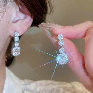 Macro shot of silver stud earrings featuring round and square sparkling zircon pendants
