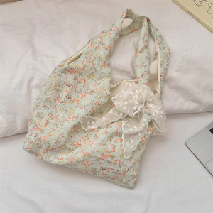 Detail view of floral canvas tote bag with white lace bow on soft white fabric background