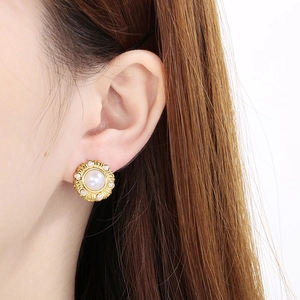 Close-up of gold round stud earring with central pearl and textured retro details