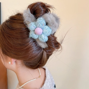 Detail of plush grey faux fur hair claw with a blue knit flower on a soft hair bun