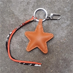 Macro detail of orange leather star keychain with fine stitching and patterned ribbon