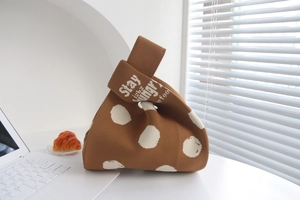 Close-up of brown knitted tote bag with white polka dots on a bright desk setting