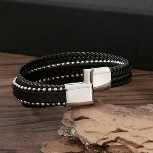 Close-up of black braided leather men's bracelet with silver metal buckle on wood