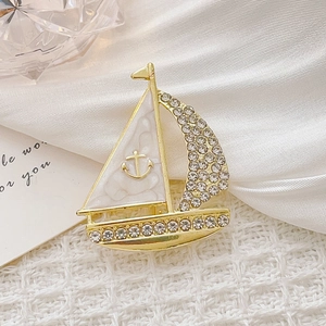 Dettaglio macro di una spilla a forma di barca a vela dorata con strass e vela marmorizzata