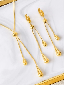 Close-up of gold teardrop pendant necklace and drop earrings on white marble tray