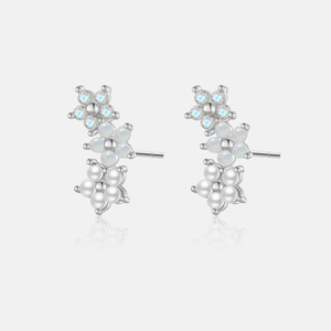 Detail of silver floral earrings with blue crystals, opals, and pearls on a grey surface