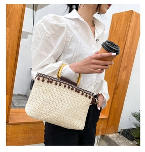 Detail of beige straw handbag featuring dark brown tassel accents and wooden handles
