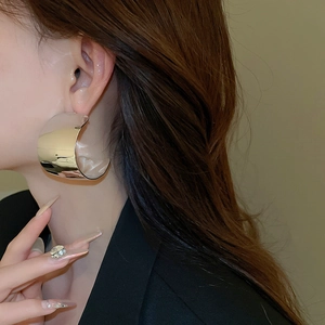 Close-up of model wearing chunky golden C-shaped hoop earrings with a polished mirror finish
