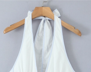 Detailansicht weißes Neckholder-Kleid mit hellblauem Rand am Holzkleiderbügel hängend
