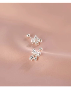 Macro shot of silver bow stud earring with lily of the valley pendant on pink satin