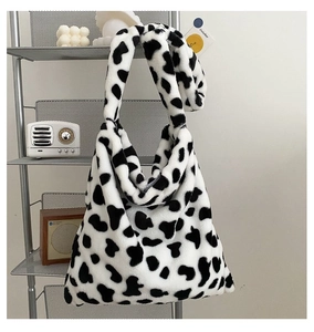 Detail of soft black and white cow print plush tote bag in a cozy home setting