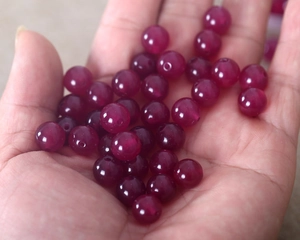 Detailed view of hand holding round purple natural stone beads for DIY jewelry making