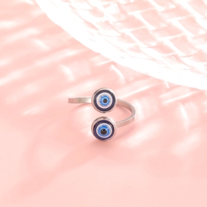 Detailed view of the silver evil eye ring with blue enamel eyes on a pink background
