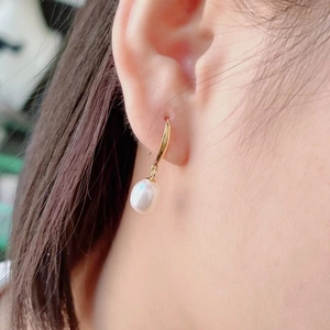 Close-up of elegant gold hook earring featuring a natural white teardrop pearl on model