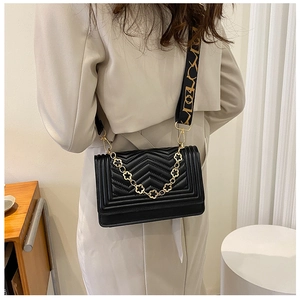 Detail of black chevron quilted crossbody bag with gold chain and printed strap on model