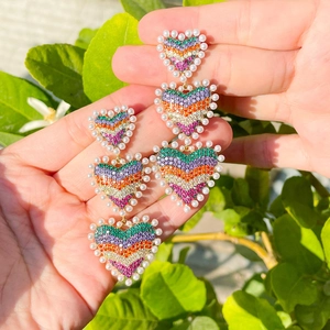 Boucles d'oreilles cœur arc-en-ciel avec zircon et perles, tenues à la main dehors