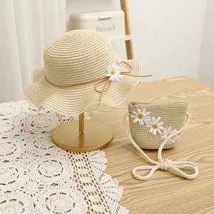 Close-up of beige straw hat and matching bag with white daisy decor on a lace tablecloth